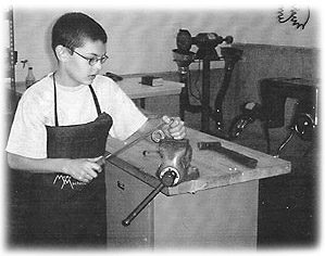 Jared, 11, in the family's home based machine shop, McArthur Machine Tool, where Jared can use simple tools, like the vise he is using.